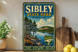 a vintage-style sign for Sibley State Park in Minnesota, with a scenic landscape of pine trees, a lake, and mountains in the background.