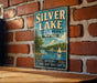 A vintage-style metal sign for Silver Lake State Park in New York, featuring a scenic illustration of a lake with a sailboat and a forested shoreline.