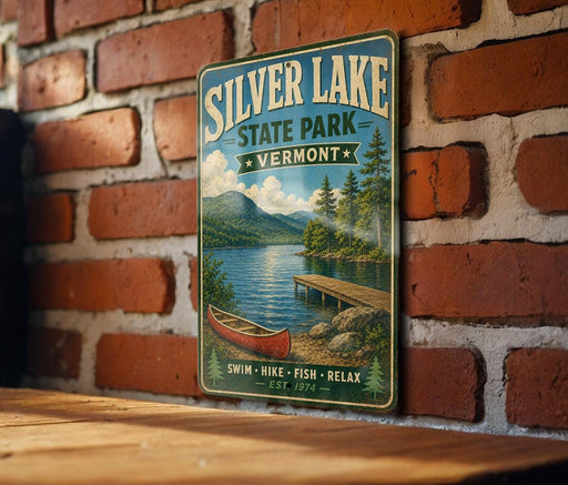 A vintage-style metal sign for Silver Lake State Park in Vermont, featuring a scenic image of a lake, mountains, and a red canoe.