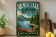 A vintage-style sign for Silver Lake State Park in Vermont, featuring a scenic image of a lake, mountains, and a canoe.