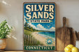 A vintage-style metal sign for Silver Sands State Park in Connecticut, featuring a beach scene with a lighthouse and a bird flying overhead.