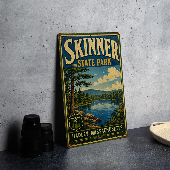 A vintage-style sign for Skinner State Park in Hadley, Massachusetts, featuring a scenic landscape with a lake and mountains.