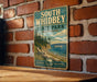 A vintage-style metal sign for South Whidbey State Park in Washington, featuring a scenic landscape with a boat on the water and a forested shoreline.