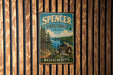 A vintage metal sign for Spencer State Forest in Massachusetts, featuring a scenic landscape with pine trees, a lake, and a sign indicating the location.