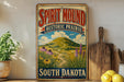 A vintage-style sign for Spirit Mound Historic Prairie in South Dakota, featuring a scenic landscape with a winding path and colorful flowers.