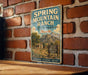 A vintage-style sign for Spring Mountain Ranch State Park in Nevada, featuring a scenic mountain landscape and a cabin, mounted on a brick wall.