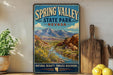 A vintage-style sign for Spring Valley State Park, Nevada, featuring a scenic mountain landscape with a river and lush vegetation.