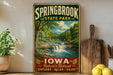 A vintage-style sign for Springbrook State Park in Iowa, featuring a scenic landscape with a waterfall and lush greenery.