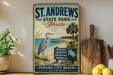 A vintage-style metal sign for St. Andrews State Park in Florida, featuring a beach scene with a heron and palm trees.