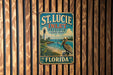 A vintage-style metal sign for St. Lucie Inlet Preserve, Florida, featuring a lighthouse and a pelican, is displayed on a wooden wall.