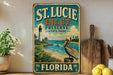 A vintage-style metal sign for St. Lucie Inlet Preserve, Florida, featuring a lighthouse and a pelican, is displayed on a shelf next to a wooden cutting board and a potted plant.