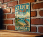 A vintage-style metal sign for St. Lucie Inlet Preserve, Florida, featuring a lighthouse and a pelican, is displayed on a brick wall.