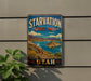 A vintage-style metal sign for Starvation State Park in Utah, featuring a scenic landscape with mountains, a lake, and a desert island.