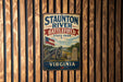 A vintage metal sign for Staunton River Battlefield State Park in Virginia, featuring an American flag and a cannon, mounted on a wooden wall.