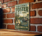 A vintage metal sign for Stephen C. Foster State Park in Georgia, featuring a portrait of a man and an illustration of a river with a steamboat.
