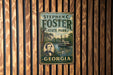 A vintage metal sign for Stephen C. Foster State Park in Georgia, featuring a portrait of a man and a depiction of the Swamp River.