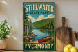 A vintage-style sign for Stillwater State Park in Vermont, featuring a scenic image of a lake, mountains, and a red canoe.