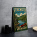 A vintage-style metal sign for Stillwater State Park in Vermont, featuring a scenic landscape with a lake, mountains, and a canoe.