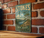 A vintage-style metal sign for Stokes State Forest in New Jersey, featuring a scenic landscape with pine trees and a lake.