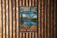 A vintage metal sign for Storrie Lake State Park in New Mexico, featuring a scenic landscape with a lake, mountains, and a Native American symbol.