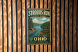 A vintage metal sign for Strouds Run State Park in Ohio, featuring a scenic landscape with a lake and mountains.