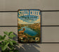 a vintage-style metal sign for Sully Creek State Park in North Dakota, with a scenic illustration of a mountain range, a river, and a ram.