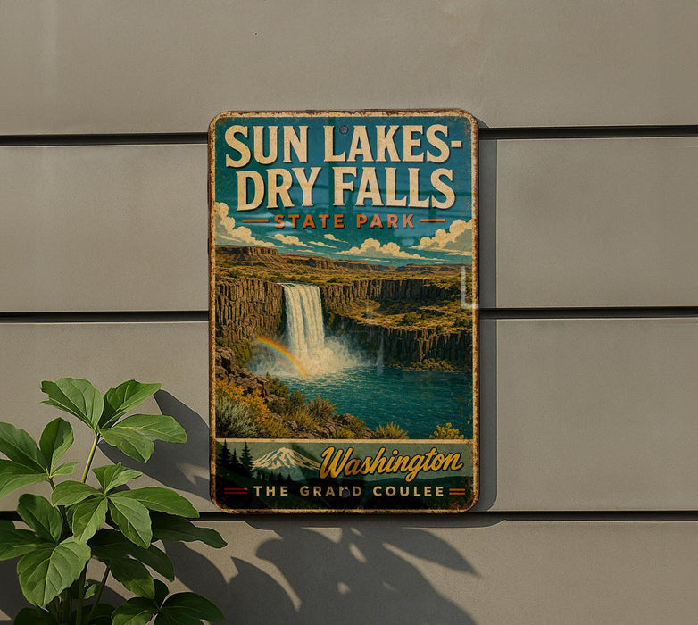 A vintage-style metal sign for Sun Lakes-Dry Falls State Park, featuring a waterfall and a mountain range, is displayed on a wall next to a plant.