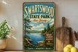 A vintage-style metal sign for Swartswood State Park in New Jersey, featuring a scenic landscape with a lake and pine trees.