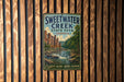 A vintage-style metal sign for Sweetwater Creek State Park in Georgia, featuring a scenic illustration of the creek and surrounding landscape.