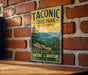 A vintage-style metal sign for Taconic State Park in New York, featuring a scenic mountain landscape and the words "Taconic State Park" prominently displayed.
