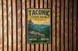 A vintage metal sign for Taconic State Park in New York, featuring a scenic mountain landscape and the words "Taconic State Park" prominently displayed.