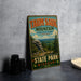 A vintage metal sign for Taung Sauk Mountain, the highest point in Missouri, with a scenic mountain landscape and pine trees.