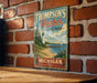 A vintage-style metal sign for "Thomson's Harbor State Park" in Michigan, featuring a lighthouse and a scenic coastal landscape.