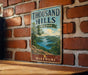 A vintage-style metal sign for Thousand Hills State Park in Missouri, featuring a scenic landscape with a lake and mountains.