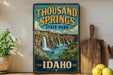 A vintage-style sign for Thousand Springs State Park in Idaho, featuring a scenic illustration of a waterfall surrounded by lush greenery.