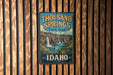 A vintage-style sign for Thousand Springs State Park in Idaho, featuring a scenic illustration of a waterfall and lush vegetation.