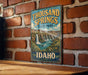 A vintage-style sign for Thousand Springs State Park in Idaho, featuring a scenic illustration of a waterfall surrounded by lush greenery.