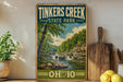 A vintage-style sign for Tinkers Creek State Park in Ohio, featuring a scenic landscape with a river, trees, and a waterfall.