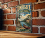 A vintage-style metal sign for Tombbee State Park in Mississippi, featuring a scenic image of a river and a canoe, mounted on a brick wall.