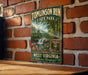 A vintage-style metal sign for Tomlinson Run State Park in West Virginia, featuring a scenic landscape with a waterfall and lush greenery.