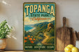 A vintage-style metal sign for Topanga State Park in California, featuring a scenic landscape with mountains, desert, and flowers.