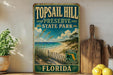 A vintage-style metal sign for Top sail Hill Preserve State Park in Florida, featuring a beach scene and a palm tree.