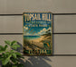 A vintage-style metal sign for Topsail Hill Preserve State Park in Florida, featuring a beach scene and palm trees.