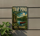 A vintage-style metal sign for Trap Pond State Park in Delaware, featuring a scenic illustration of a pond with a canoe and trees.