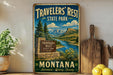 A vintage-style metal sign for Travelers' Rest State Park in Montana, featuring a scenic landscape with mountains, a river, and a stone signpost.