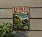 A vintage-style metal sign advertising turkey bluffs in Illinois, featuring a turkey, a river, and lush greenery.