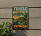 A vintage-style sign for Turtle Mound National Historic Landmark in Florida, featuring a turtle and a tropical landscape.