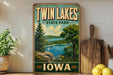 A vintage-style sign for Twin Lakes State Park in Iowa, featuring a scenic landscape with a lake, mountains, and a sailboat.
