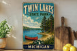 A vintage-style sign for Twin Lakes State Park in Michigan, featuring a scenic image of a lake, pine trees, and a red canoe.