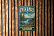 A vintage-style metal sign for Twin Lakes State Park in Virginia, featuring a scenic landscape with pine trees, a lake, and mountains.